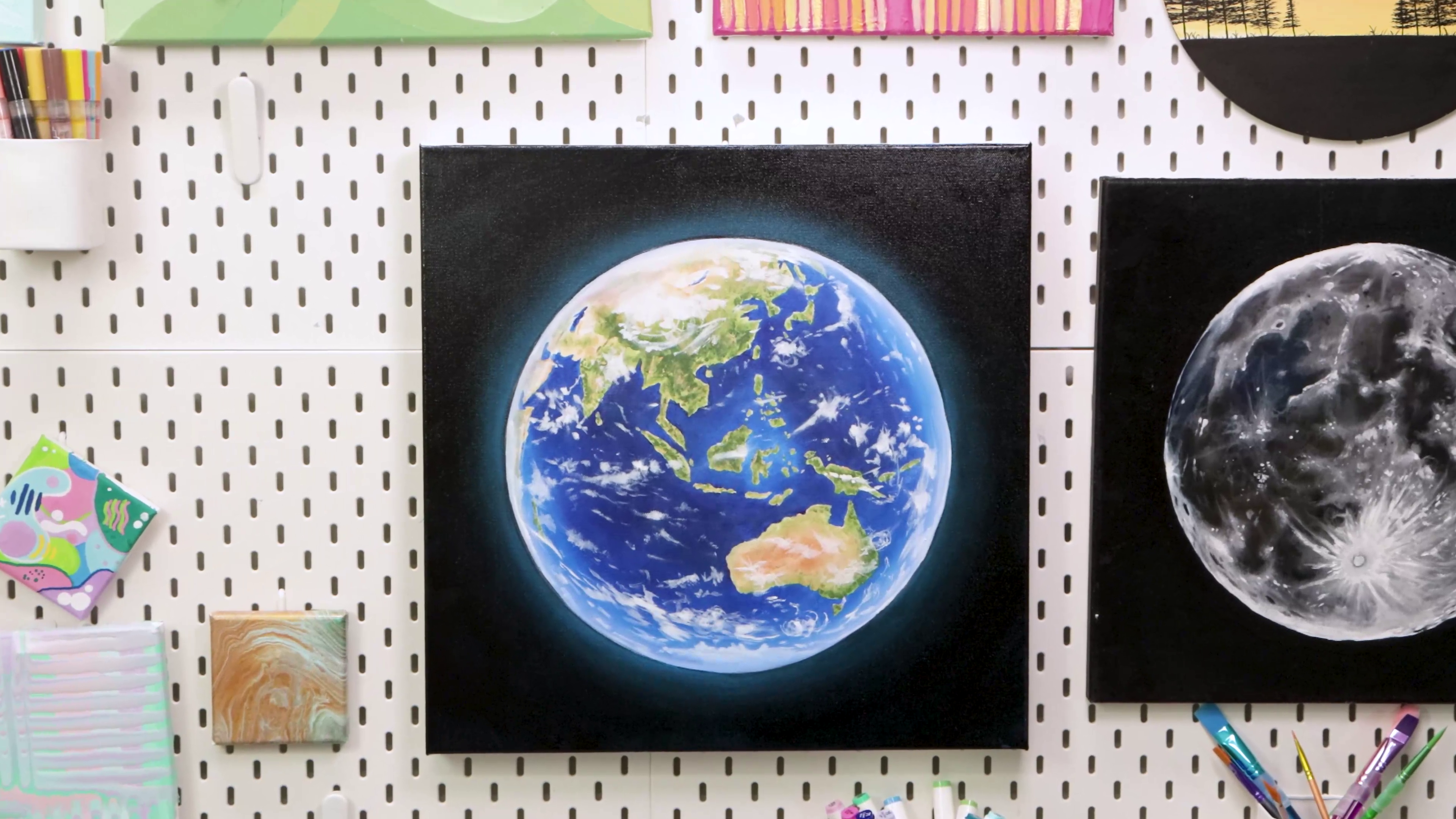 Final earth painting hung on pegboard around other art