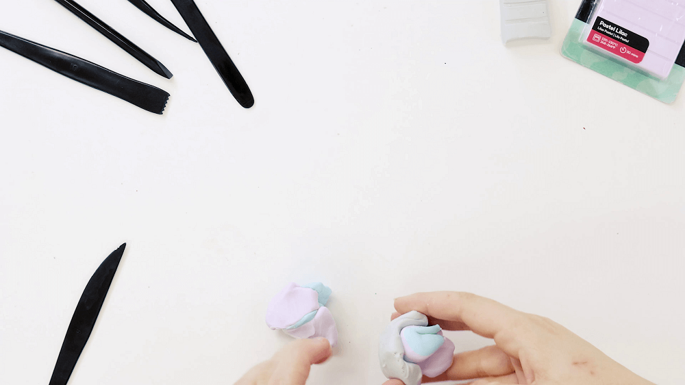 A hand rolls pastel blue, pastel pink and silver Make n Bake Polymer clay together to form a ball.