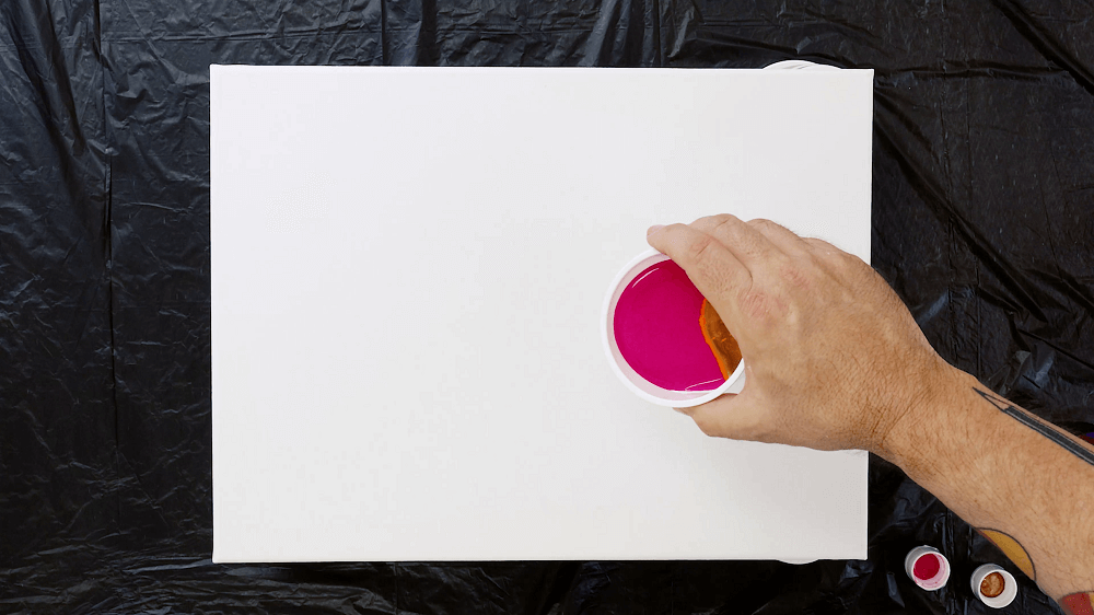 Hand holding a plastic cup pours layered coral pour painting. 