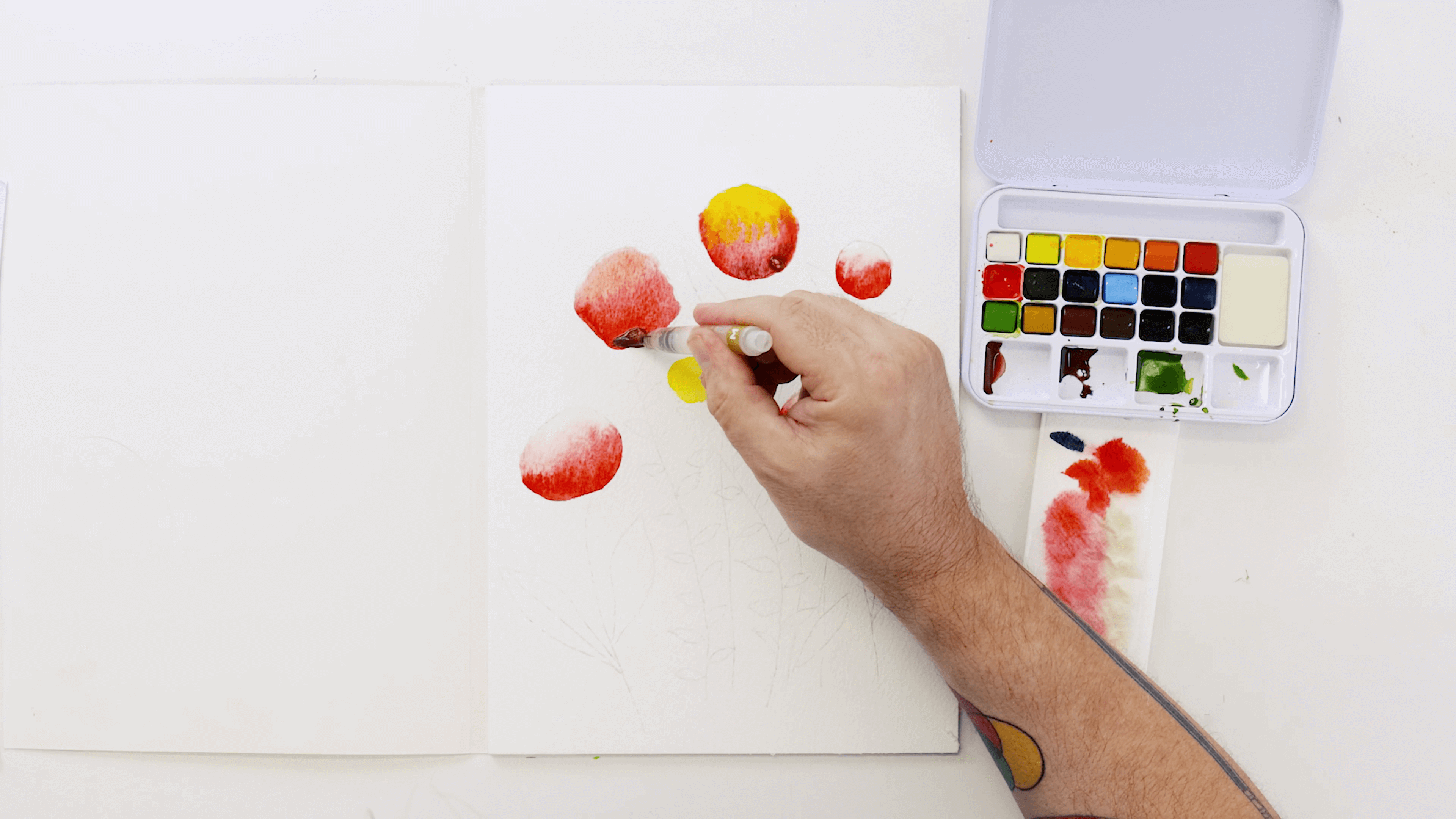 A hand holding a watercolour brush adds the colour Ultramarine blue to darken the flowers.