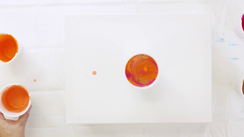 Bird's eye view of a plastic cup filled with orange, pink and coral pour paints.