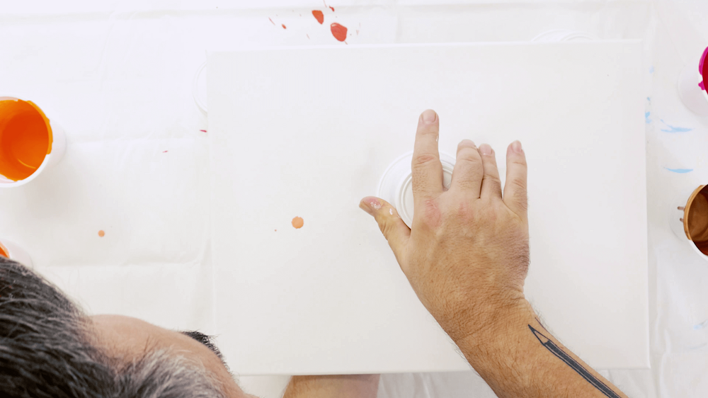 Man flips plastic cup upside down on top of a clean canvas to create a pour painting.