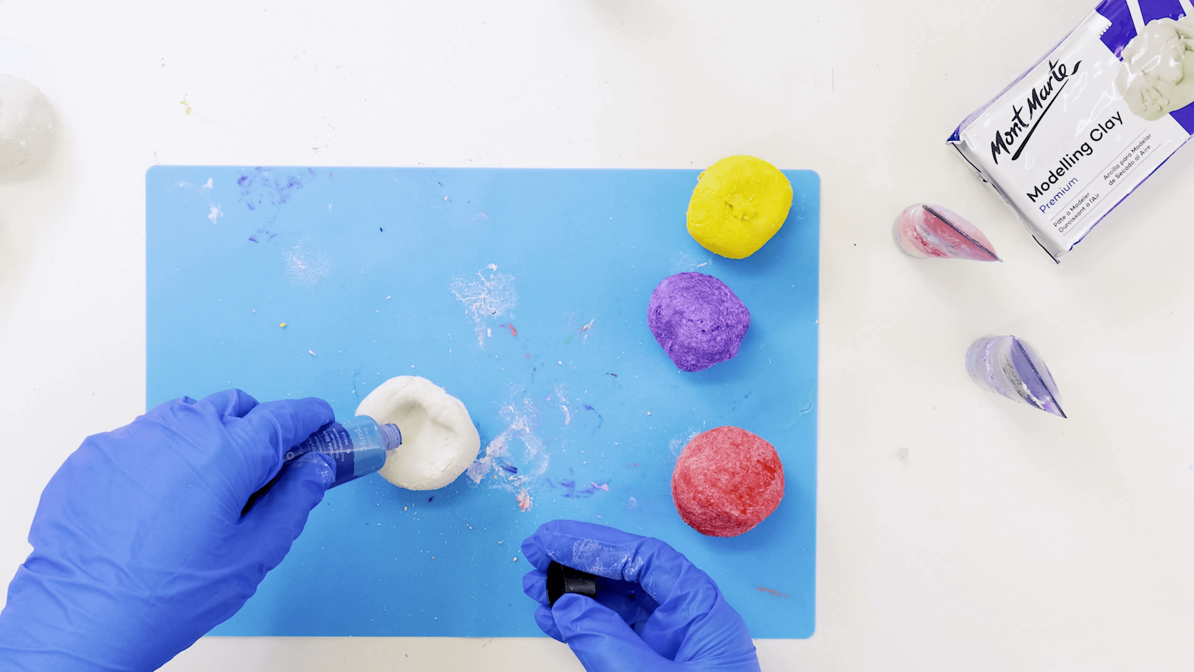 Hand wearing blue gloves squeezing blue acrylic paint colour into a ball of air dry clay