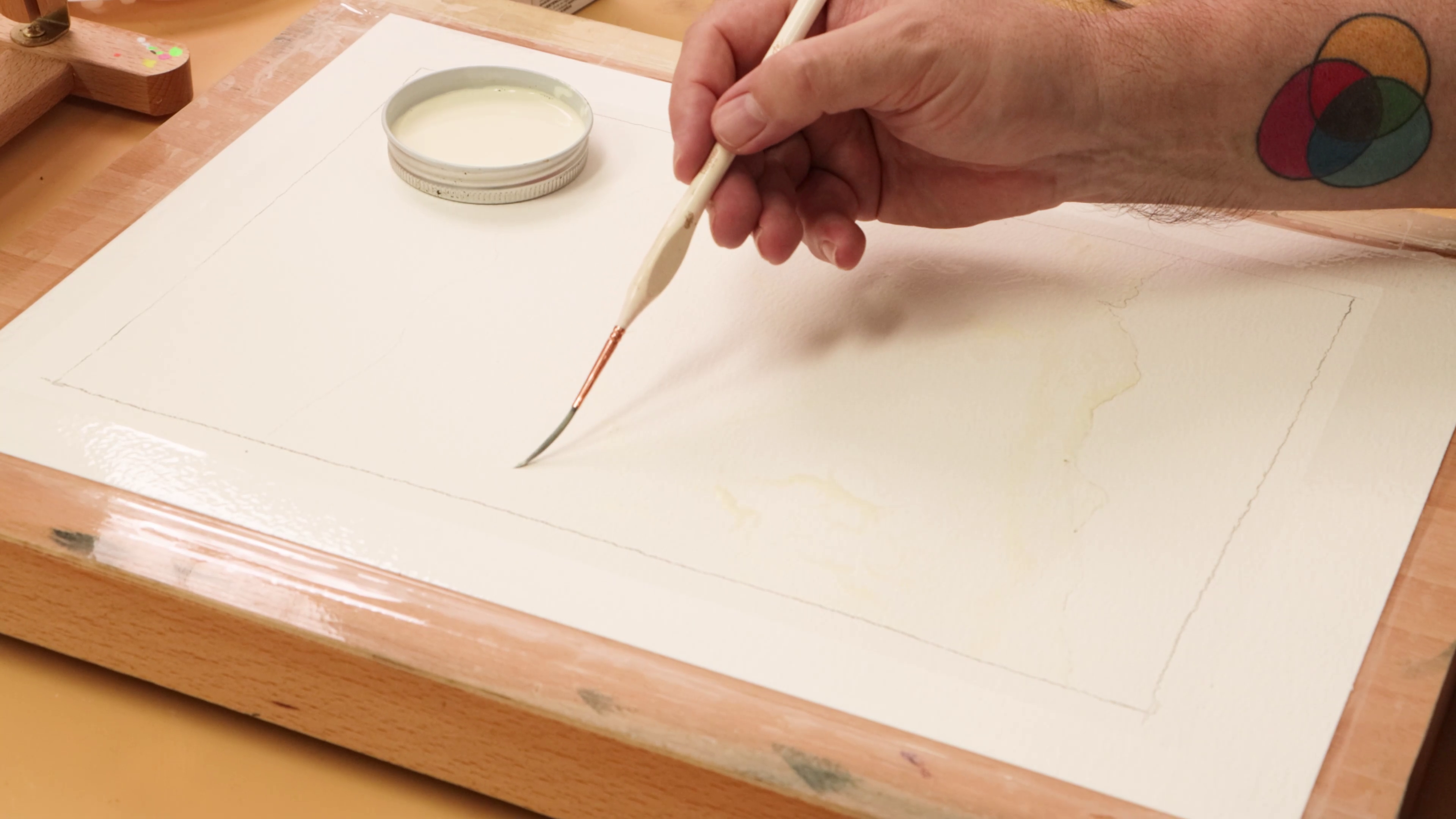 Masking fluid being applied with a liner brush to the taped watercolour paper