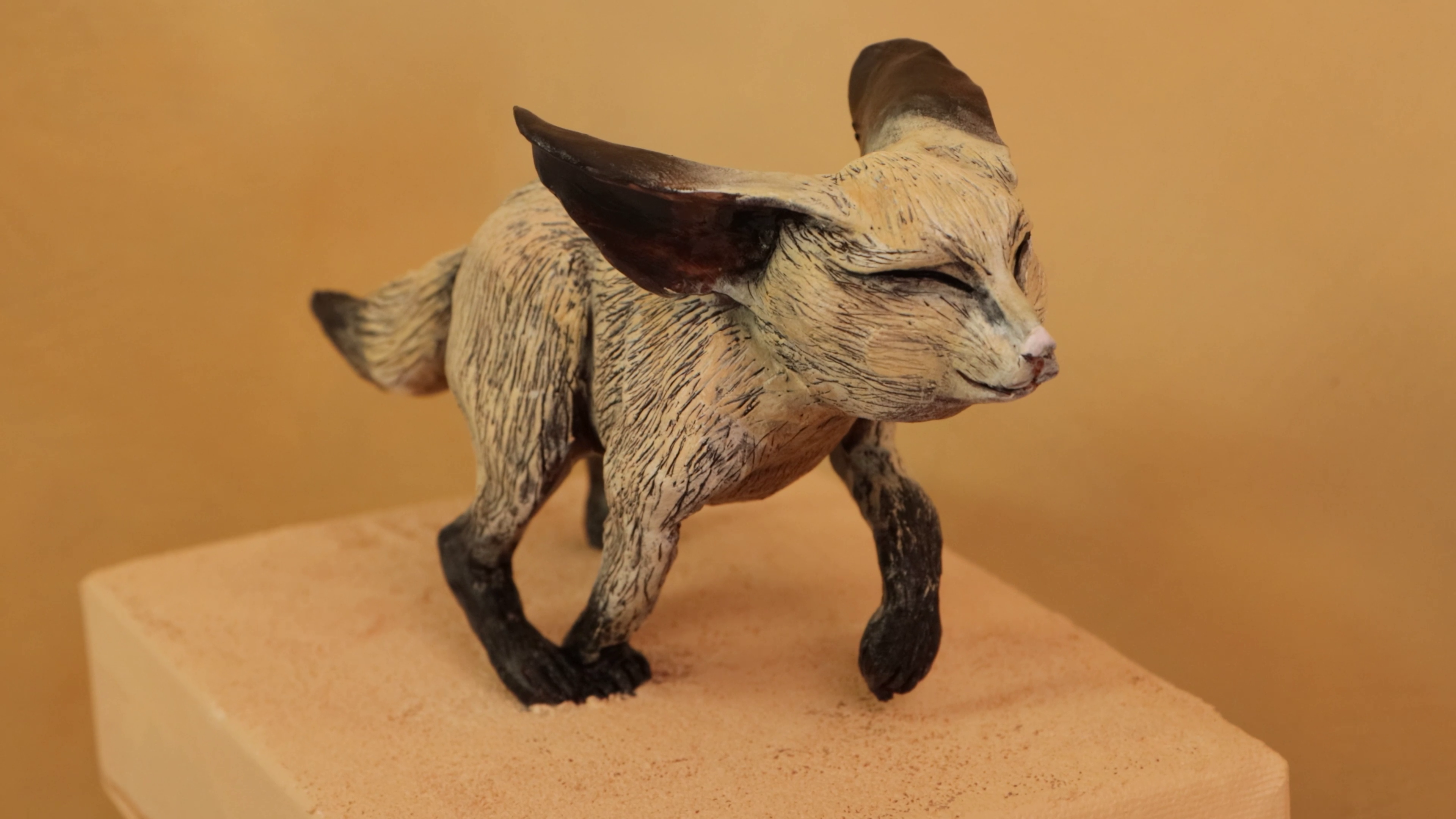 Painted polymer clay fox standing on sandy canvas base