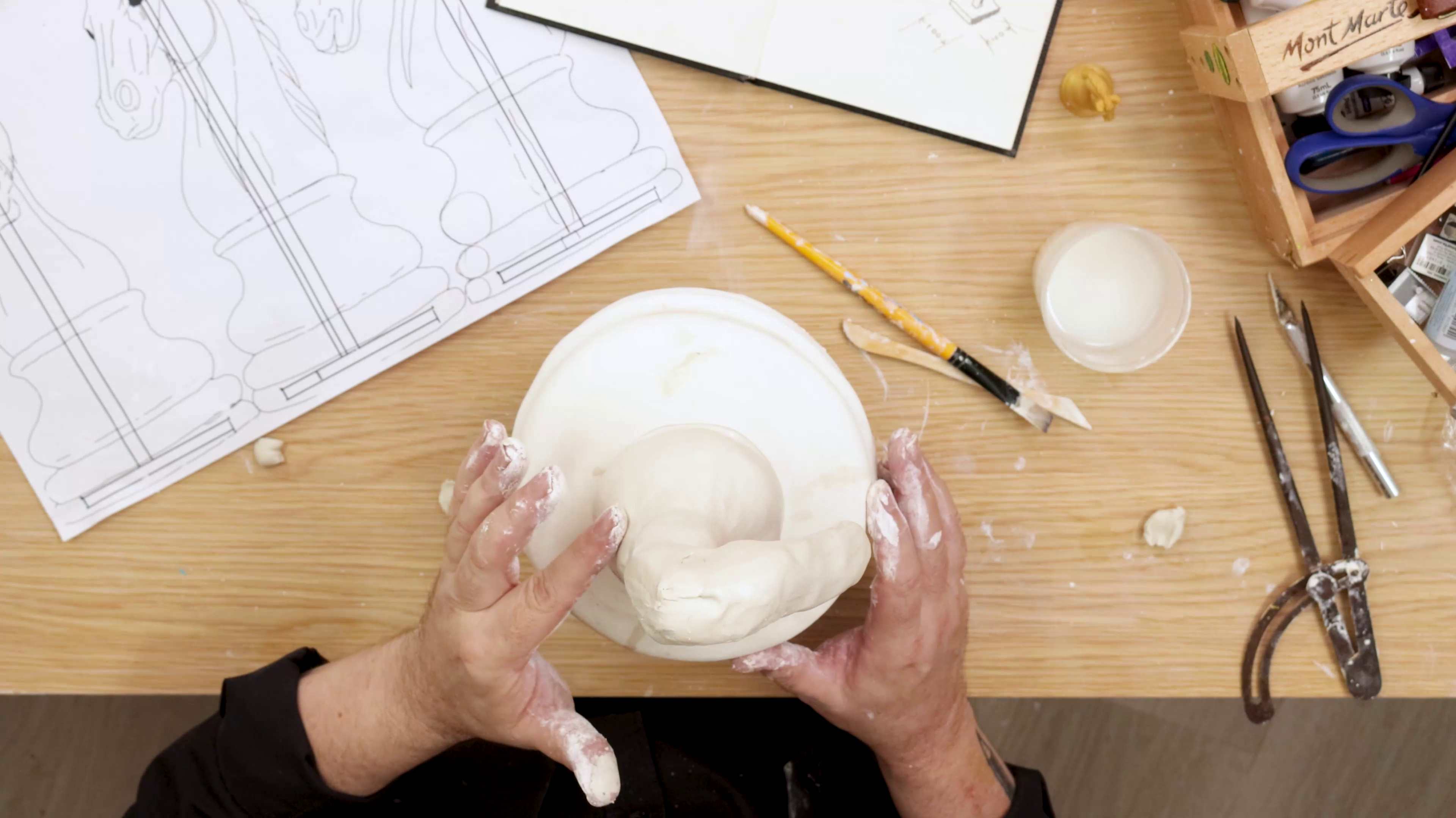 Hands smoothing clay sculpture from top view