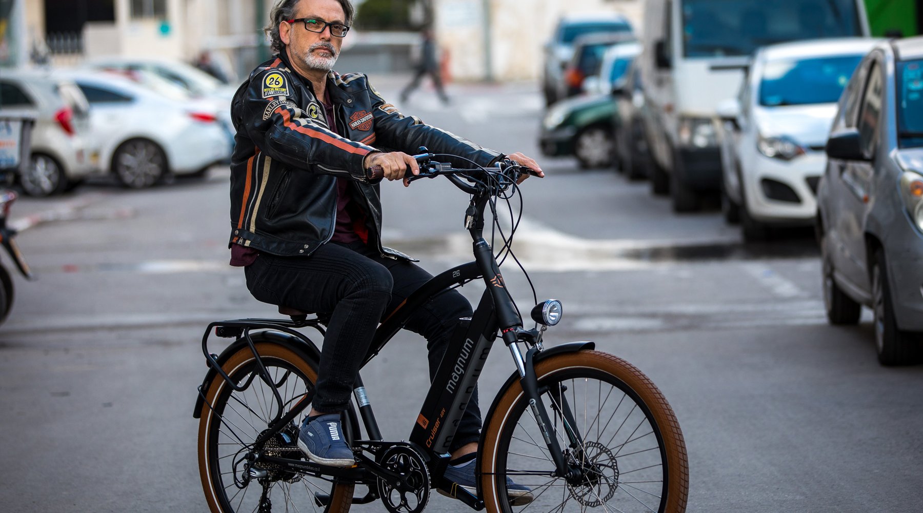 Rider in black jacket with red beige stripes on Magnum Cruiser on road with parked cars
