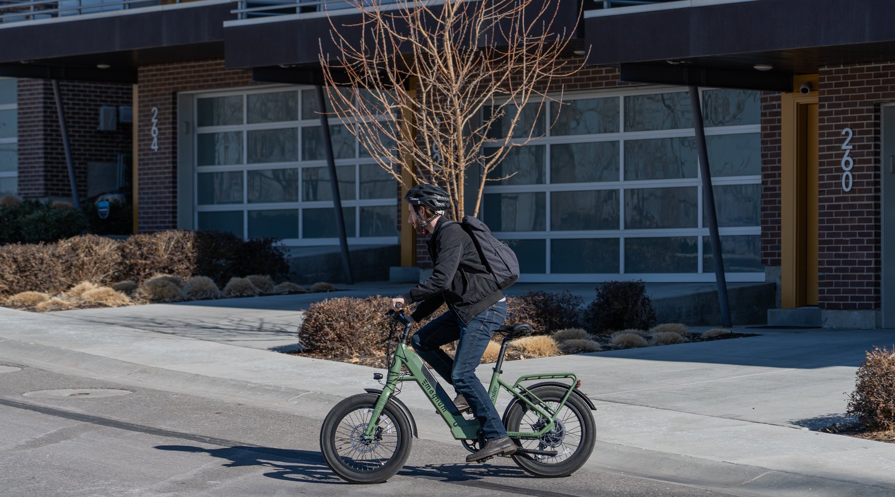 Rider with black jacket jeans and helmet riding green Magnum Pathfinder T electric bike in front of townhouses