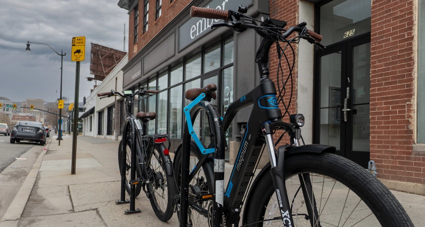 Magnum Voyager electric bike locked to bike rack on city sidewalk in front of brick building