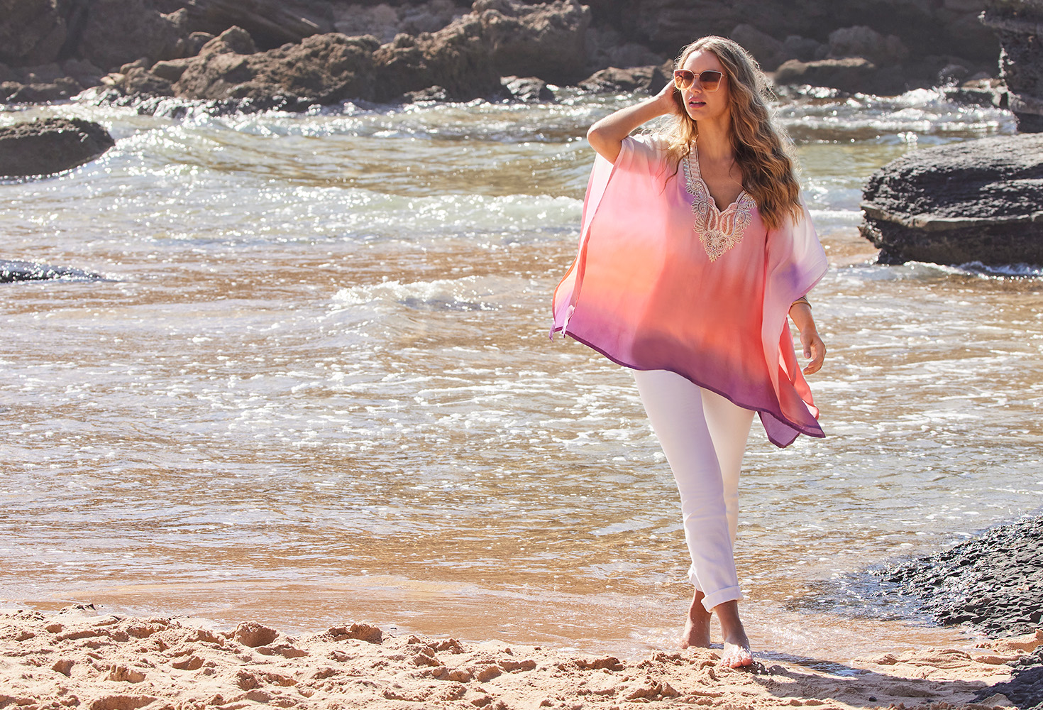 model wearing a pink ombre embellished poncho cover-up and white jeans.