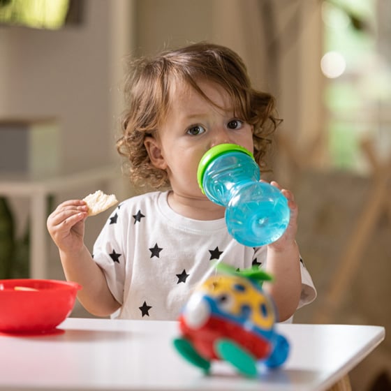 Child eating and drinking from a blue sippy cup
