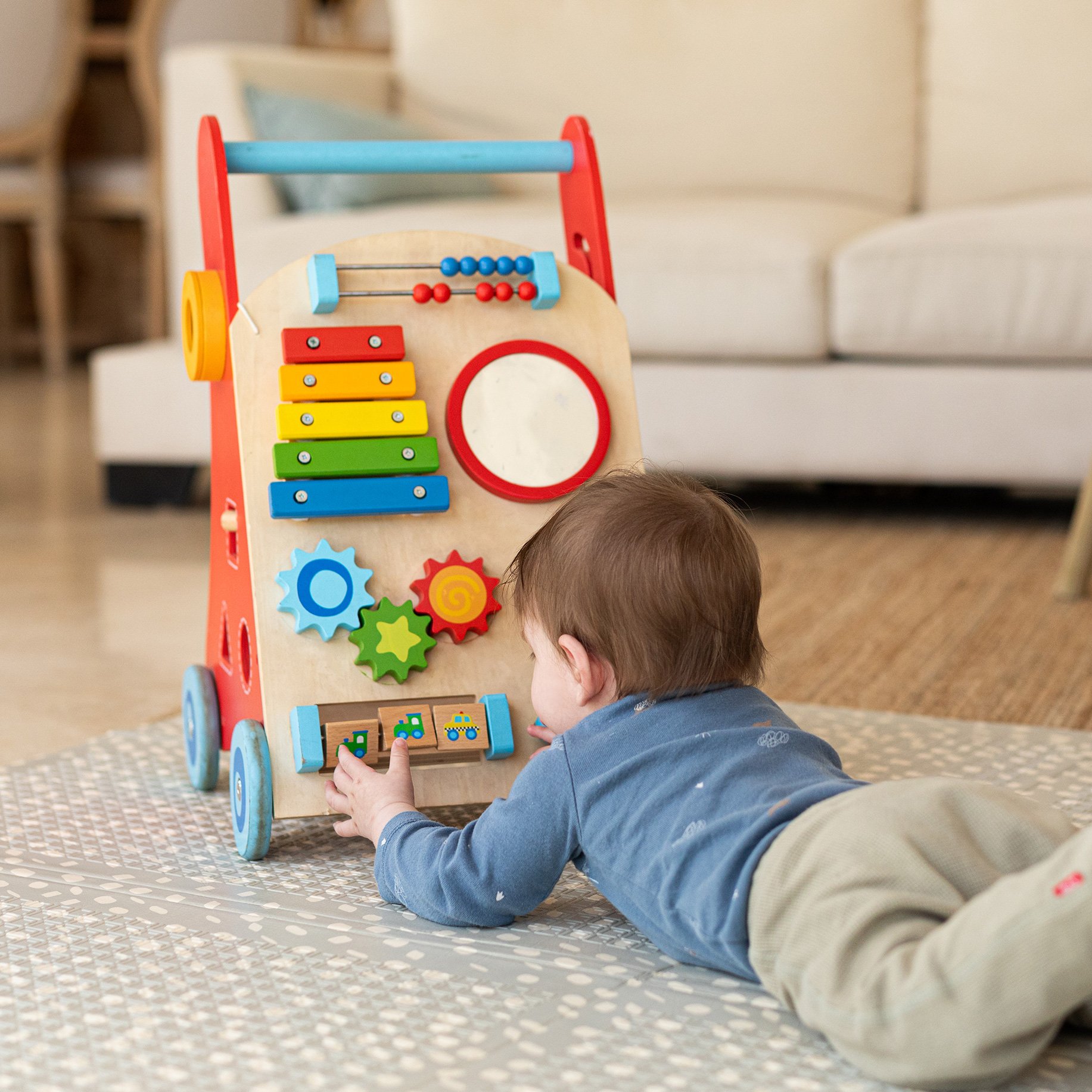 Child lying on floor playing with a Nuby Wooden Baby Walker.