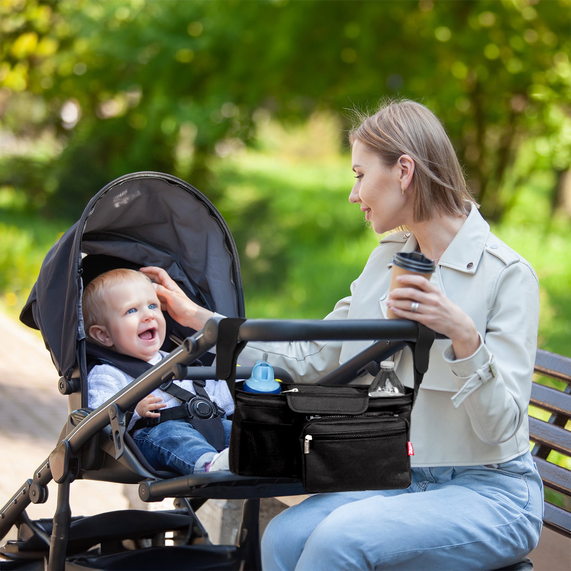 Mother on park bench playing with her baby who is laughing in a stroller.