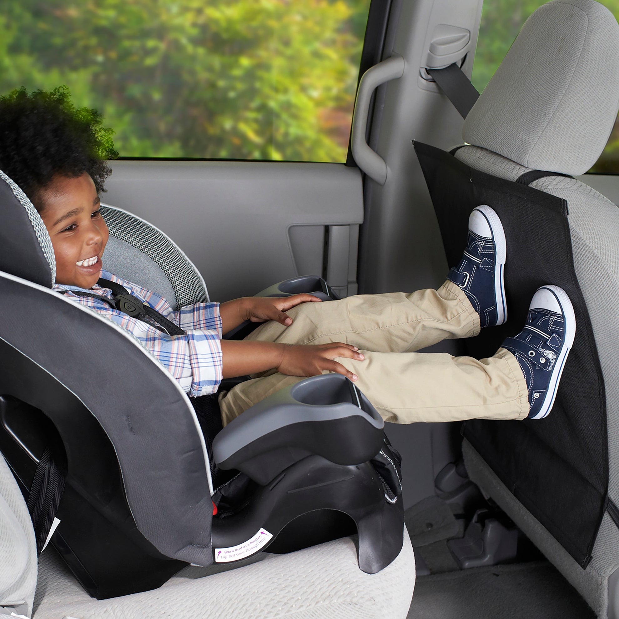 Toddler sitting in car seat with feet pressed against a Nuby Kick Mat on the seat in front of him.