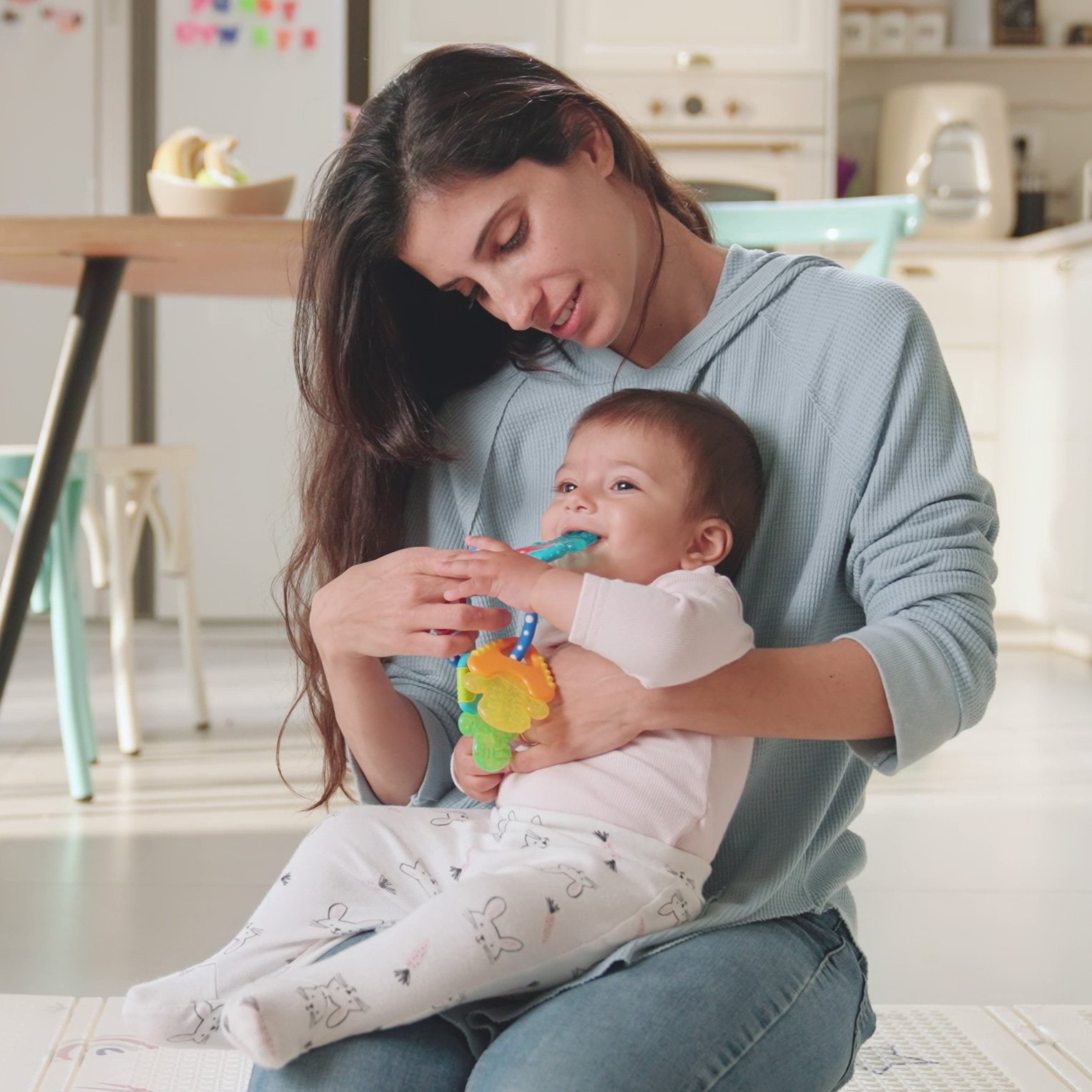 Infant sitting on mother's lap while teething on Nuby's Icybite Cooling Teether Keys