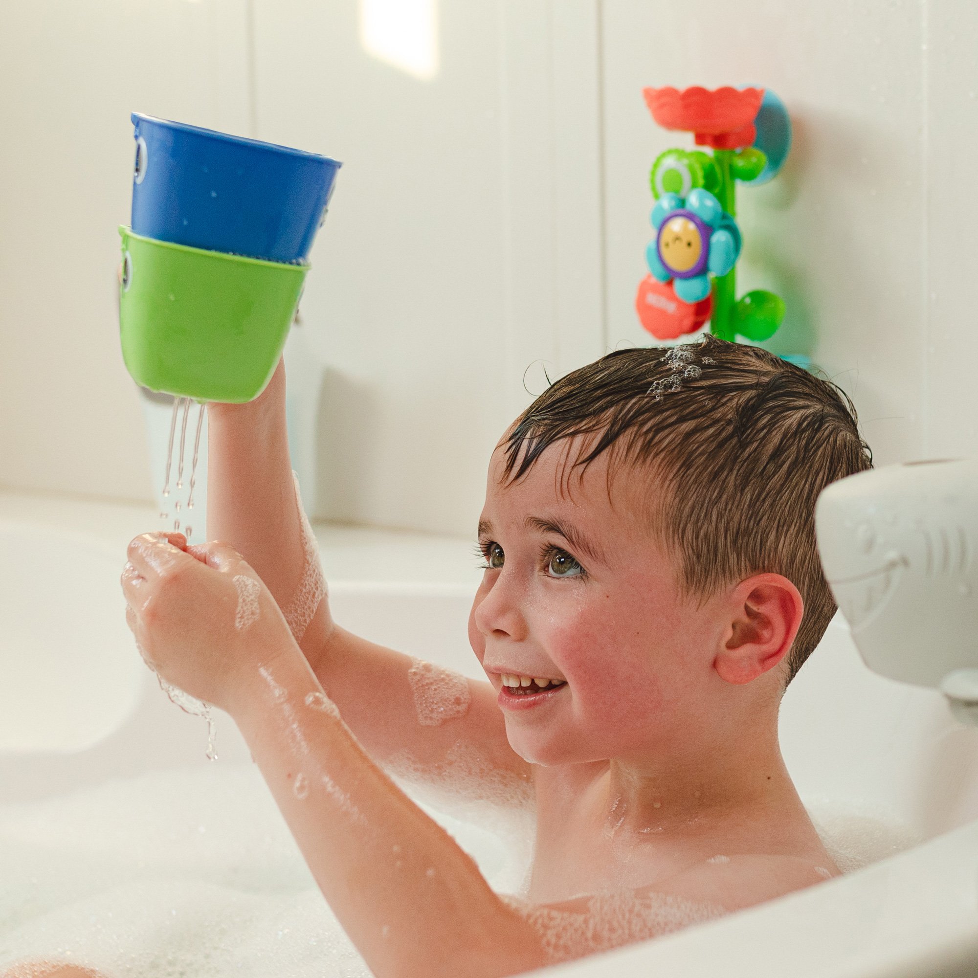 Toddler playing in bathtub with Nuby's Whale Stacking Bath Cups and Flow N' Grow Bath Toy.