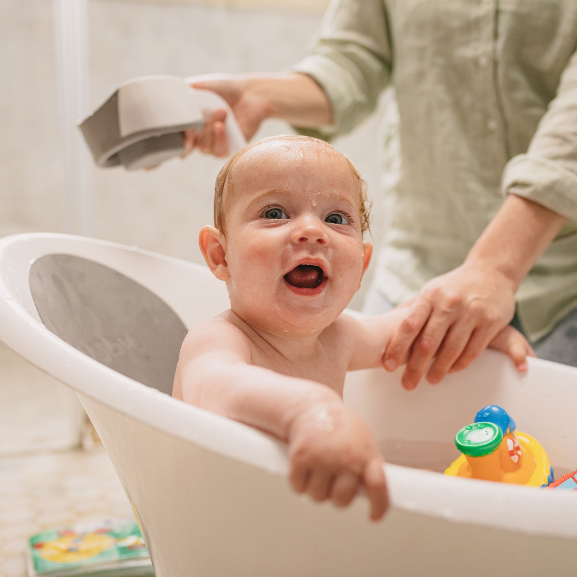 Baby getting bathed in a Nuby Sit and Bathe Compact Bathtub, playing with Tub Tugs bath toys.