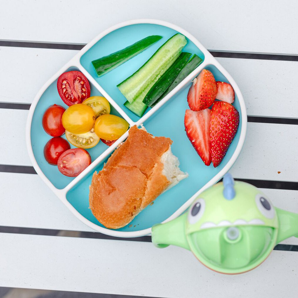 Nuby Rectangular Silicone Suction Plate in aqua holding fruits and vegetables, next to a Dino Clik-It Silicone Straw Trainer Cup.