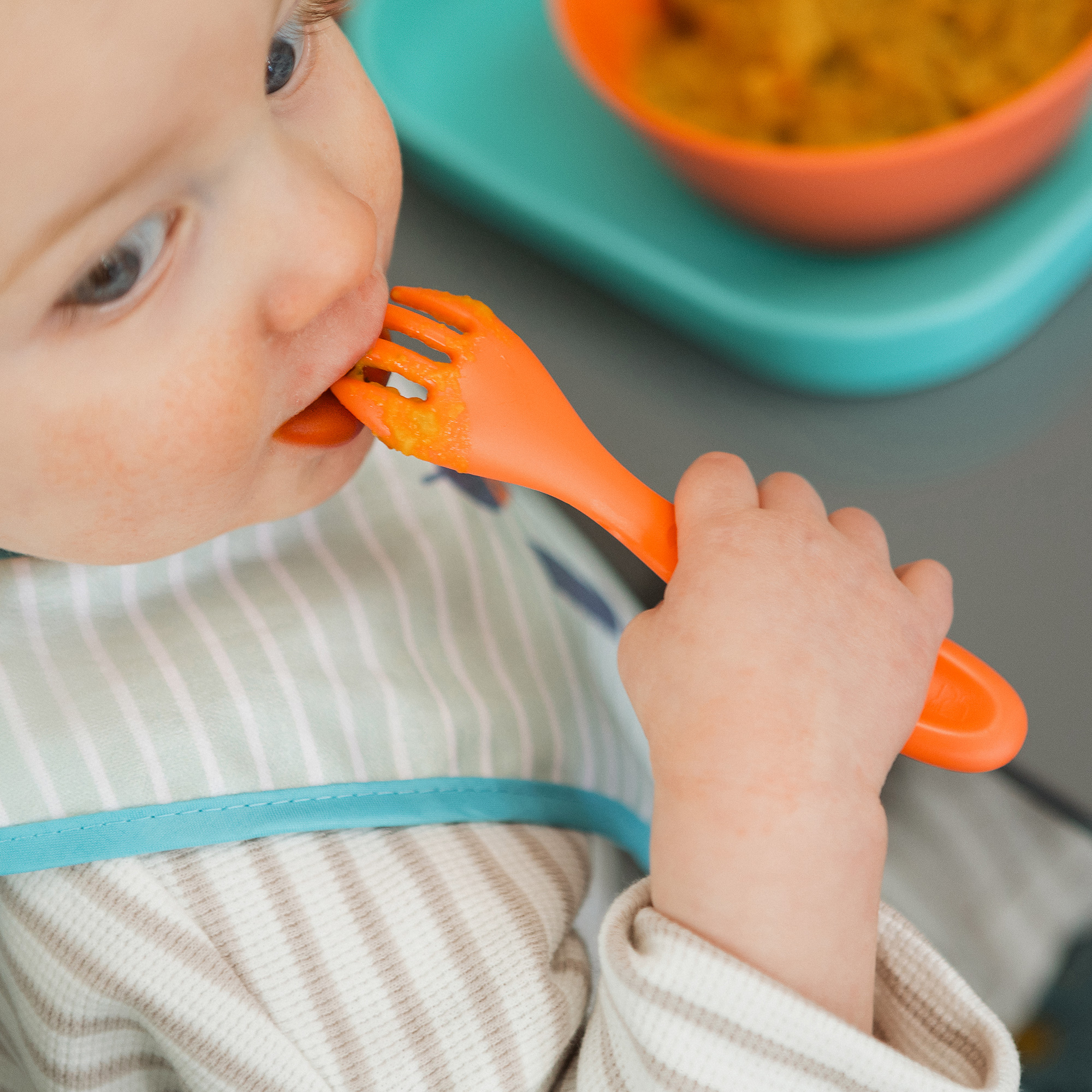 Toddler eating at mealtime using an orange Nuby fork.