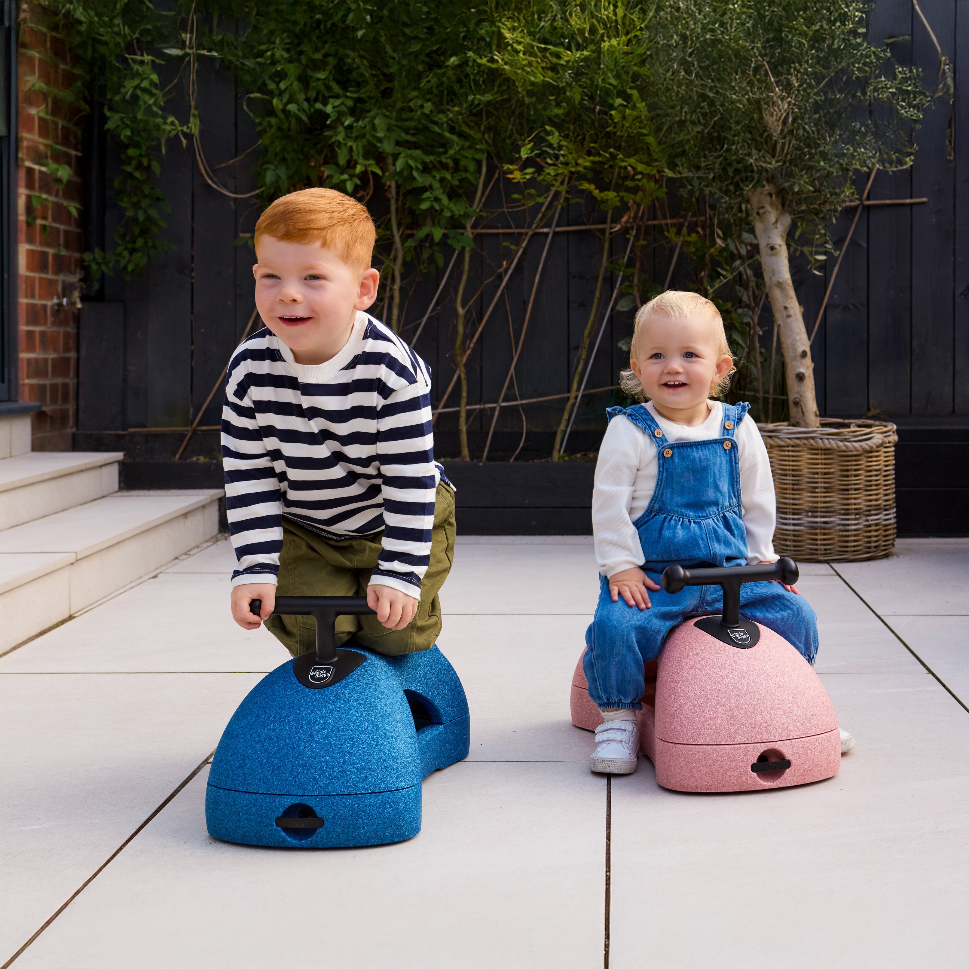 Two children playing with Nuby Boogie Buggy sit and ride while outside.