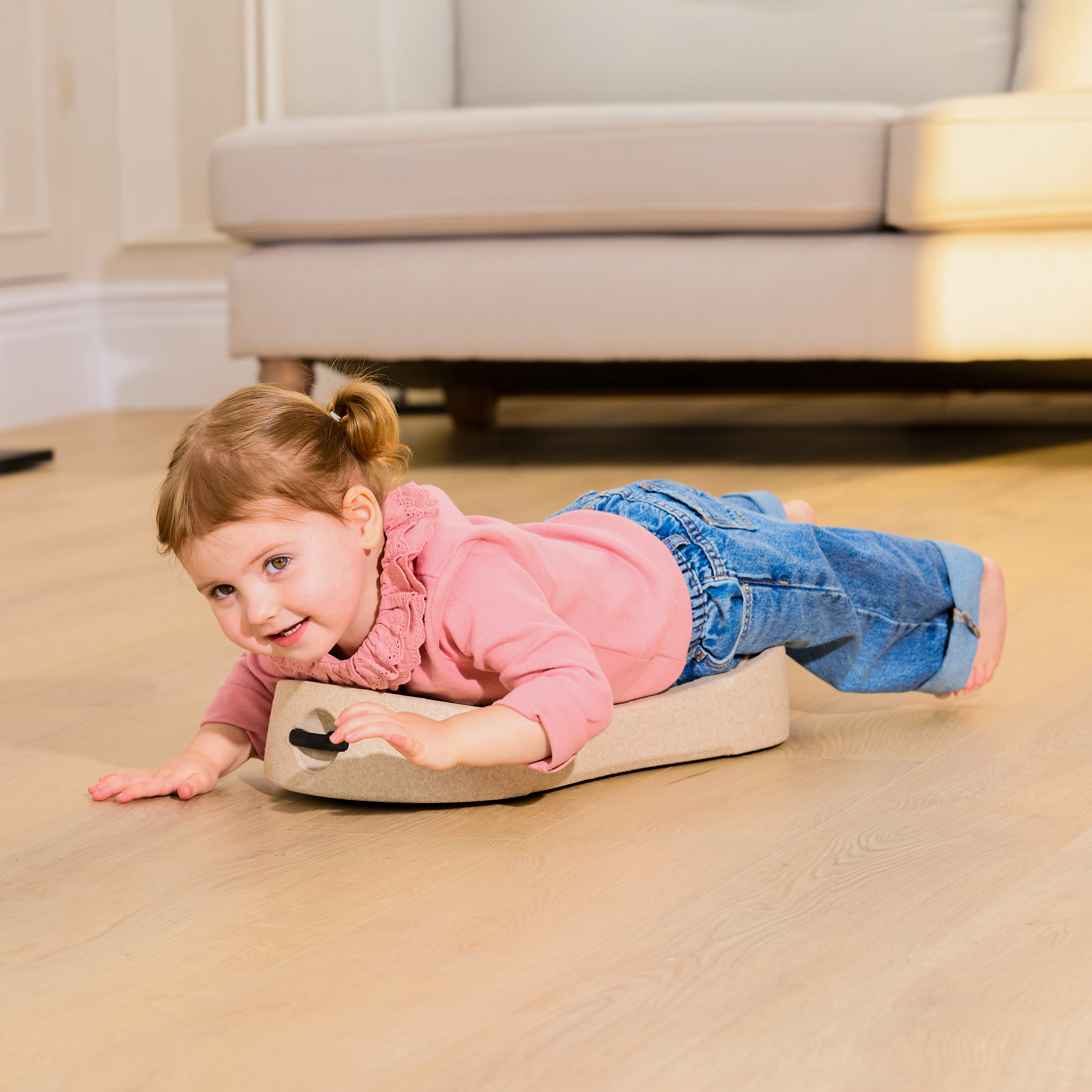 Child playing with Nuby Rock 'N Ride caster board, rolling across the living room floor.