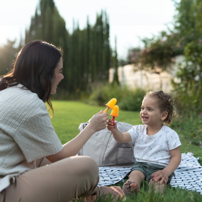 Toddler eating an Animal Ice Pop Mold fruit popsicle with mom outside.