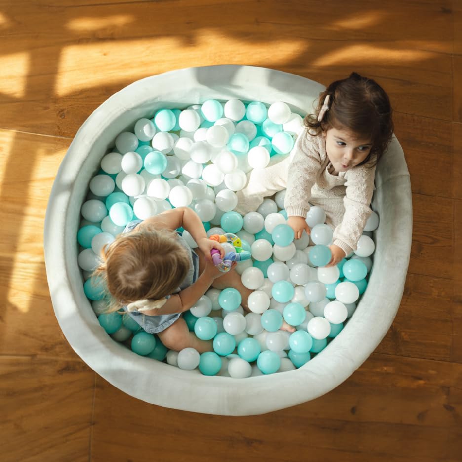 Two young girls playing in a grey Nuby ball pit with blue and white balls.