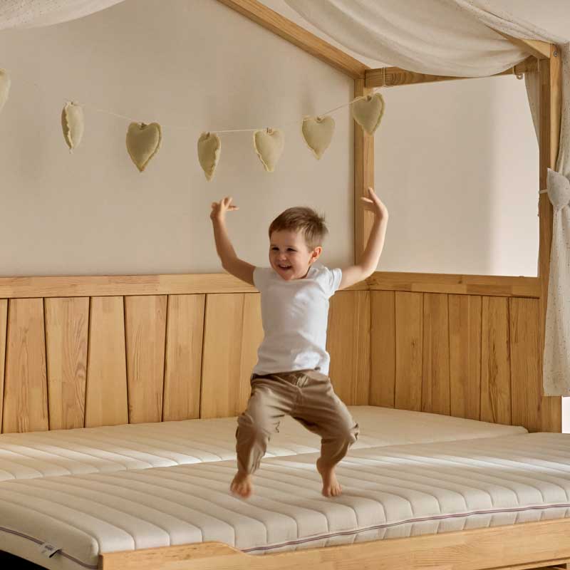 un enfant saute sur un matelas 90 x 190 de lit cabane. Il porte un pantalon beige et un t-shirt blanc. Enfant qui saute sur un lit