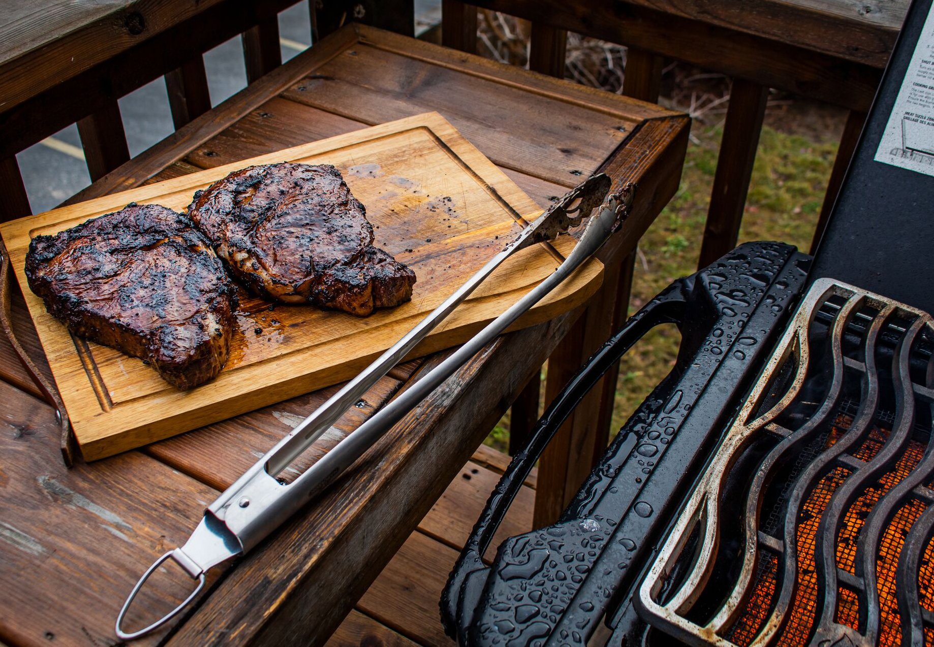 Grilled steaks resting on cutting board near BBQ.