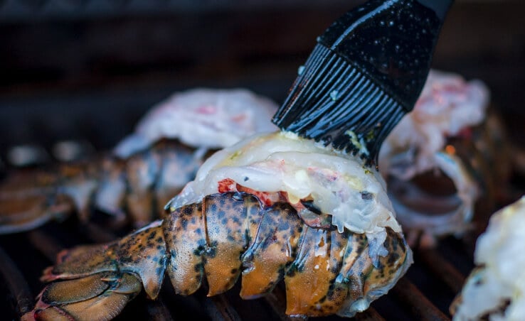 Grilling lobster tail basted with butter by brush.