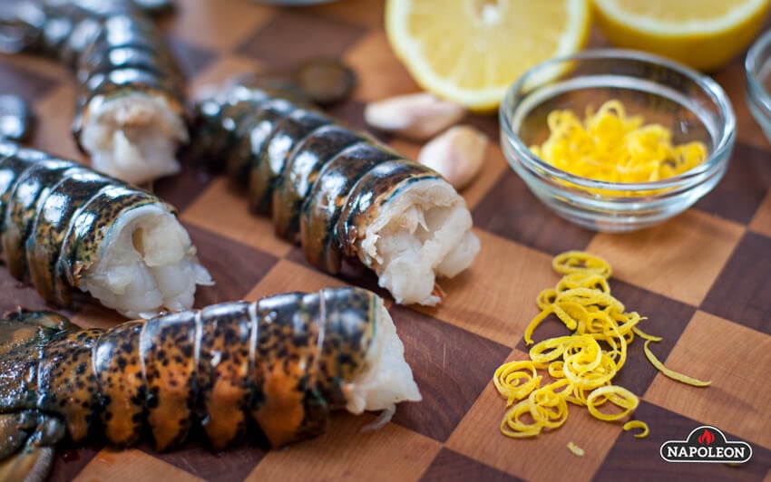 Raw lobster tail and lemon zest resting on cutting board.