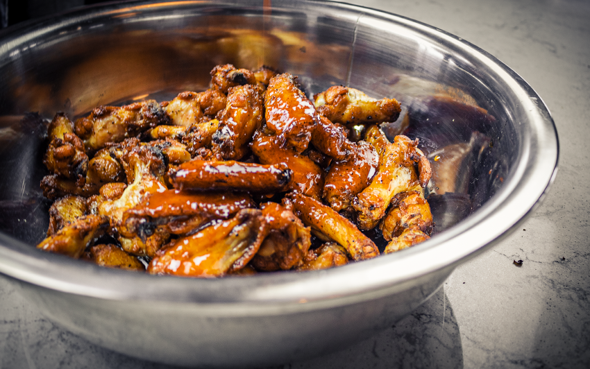 Grilled chicken wings inside metal bowl and covered in sauce.