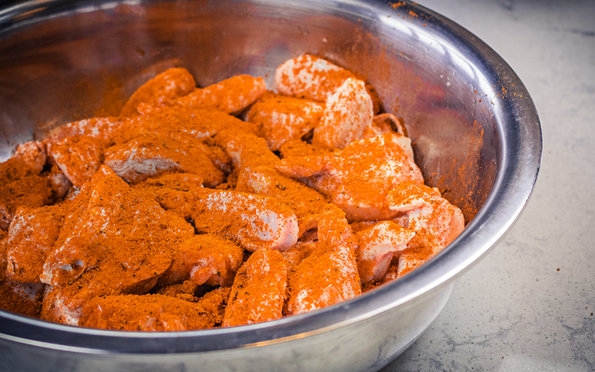 Raw chicken wings in metal bowl covered in spices.