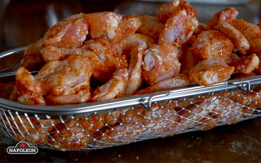 Raw chicken wings covered in spice inside rotisserie basket.