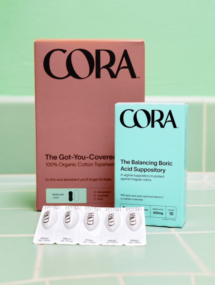 Cora's Boric Acid Suppository and menstrual liners sitting upright on a tiled surface 