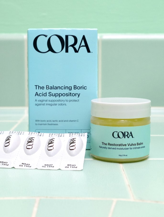 Cora's Boric Acid Suppository and Restorative Vulva Balm sitting upright on a tile surface